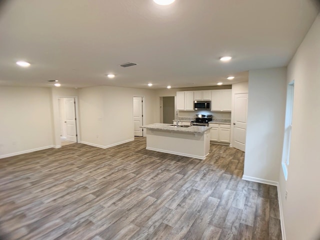 kitchen featuring a center island with sink, visible vents, light stone countertops, stainless steel appliances, and white cabinetry