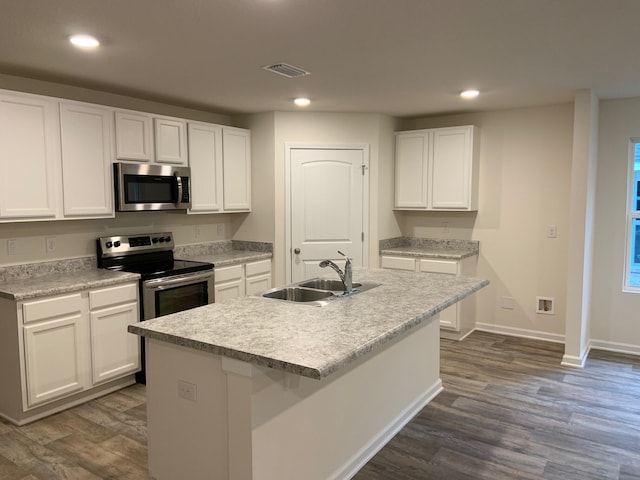 kitchen with appliances with stainless steel finishes, white cabinets, light countertops, and an island with sink