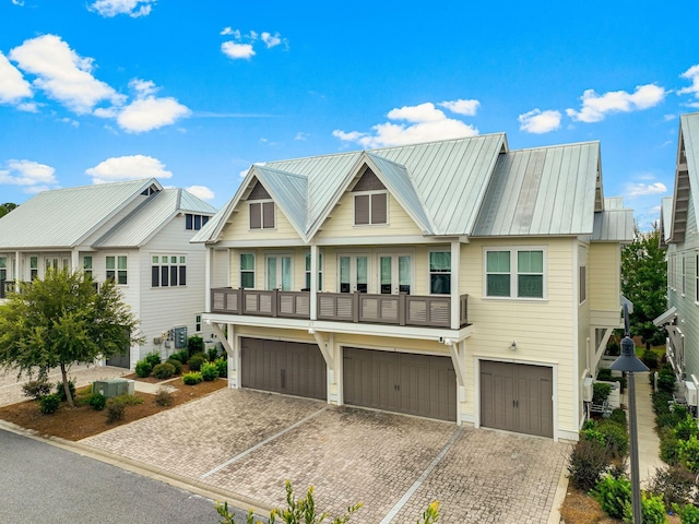 view of front of house with a balcony, metal roof, an attached garage, a standing seam roof, and decorative driveway