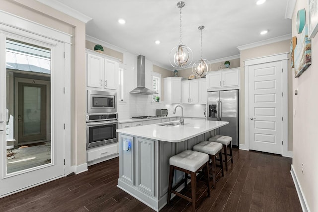 kitchen featuring white cabinets, ornamental molding, stainless steel appliances, wall chimney range hood, and a sink