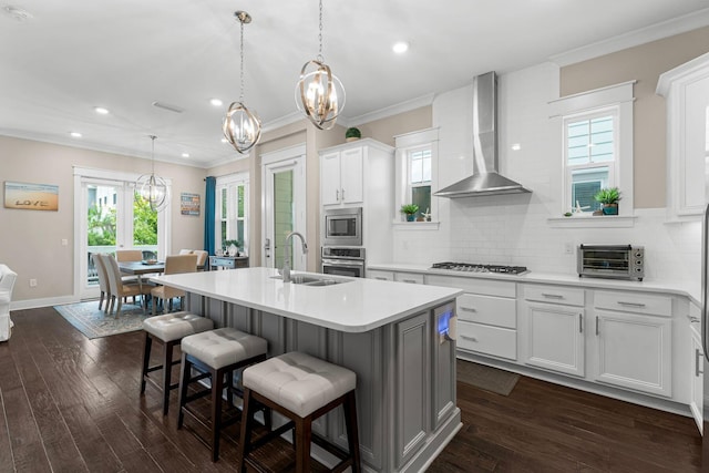 kitchen with a toaster, a sink, light countertops, wall chimney range hood, and appliances with stainless steel finishes