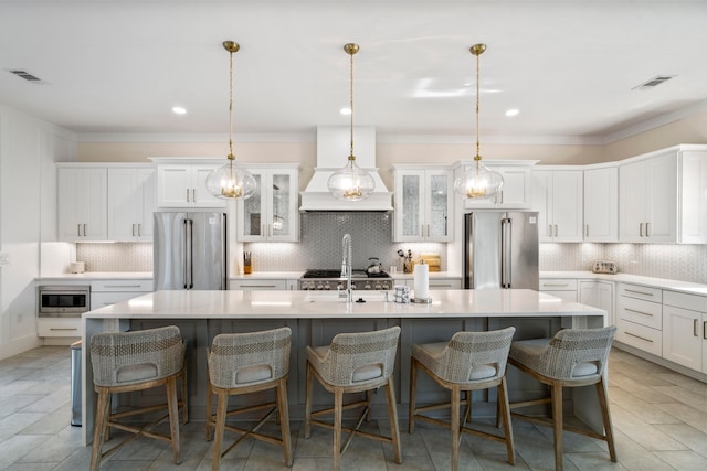 kitchen featuring decorative backsplash, premium range hood, an island with sink, and stainless steel appliances