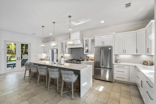 kitchen with a center island with sink, custom exhaust hood, freestanding refrigerator, decorative backsplash, and light countertops