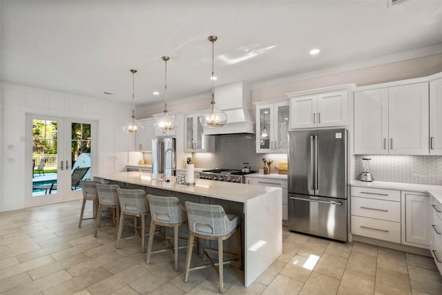 kitchen with custom exhaust hood, tasteful backsplash, a center island with sink, and stainless steel fridge