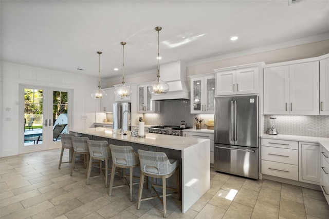 kitchen featuring high quality fridge, light countertops, a center island with sink, tasteful backsplash, and custom range hood