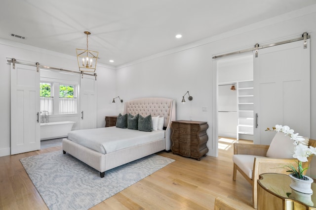 bedroom with a notable chandelier, light hardwood / wood-style flooring, a barn door, and ornamental molding