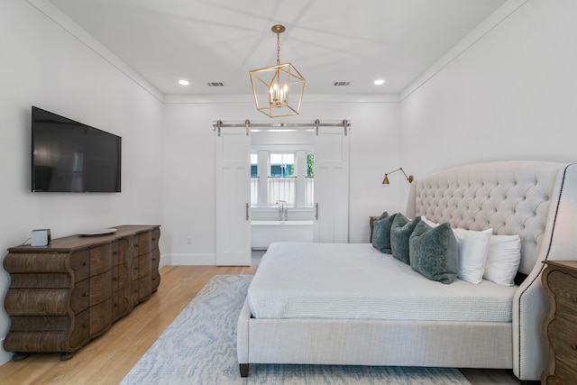 bedroom featuring ornamental molding, an inviting chandelier, light wood-type flooring, and a barn door