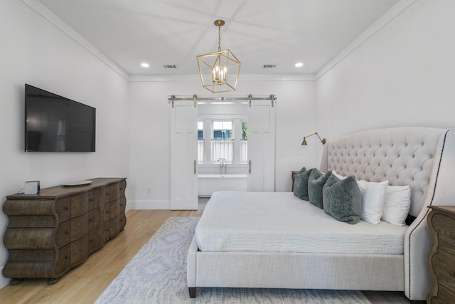 bedroom with a barn door, light wood-style flooring, visible vents, and crown molding