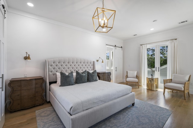bedroom featuring a barn door, visible vents, a chandelier, wood finished floors, and crown molding