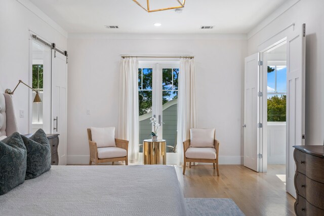 bedroom with multiple windows, ornamental molding, wood-type flooring, and a barn door