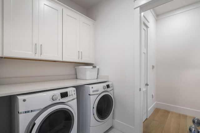 clothes washing area with light wood-type flooring, baseboards, washer and dryer, and cabinet space