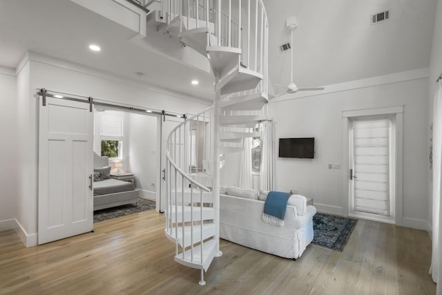 stairway featuring a barn door, wood finished floors, visible vents, a ceiling fan, and baseboards