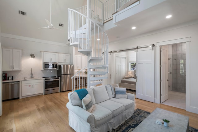 living room with ceiling fan, a barn door, a high ceiling, light hardwood / wood-style floors, and sink