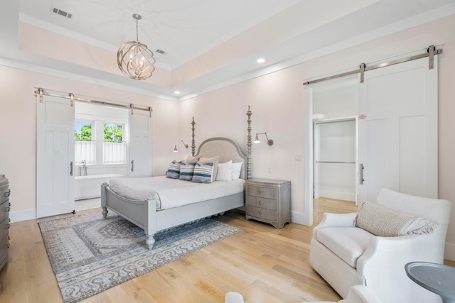 bedroom featuring light hardwood / wood-style floors, a raised ceiling, and a barn door