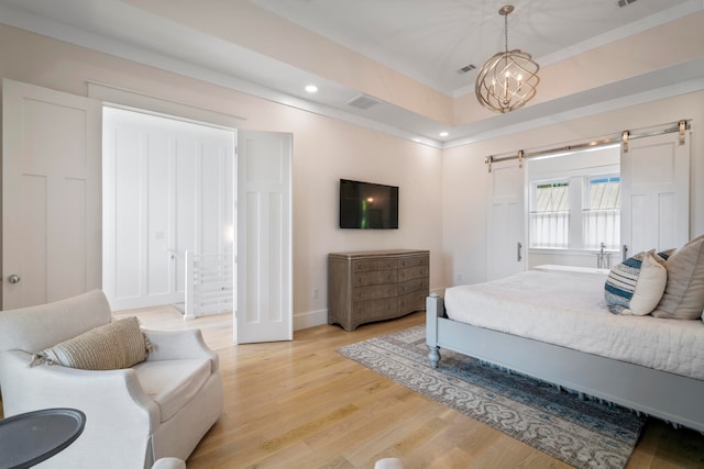 bedroom featuring a raised ceiling, light hardwood / wood-style flooring, a barn door, and a chandelier