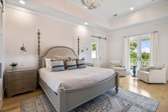 bedroom featuring a raised ceiling, wood-type flooring, and a barn door