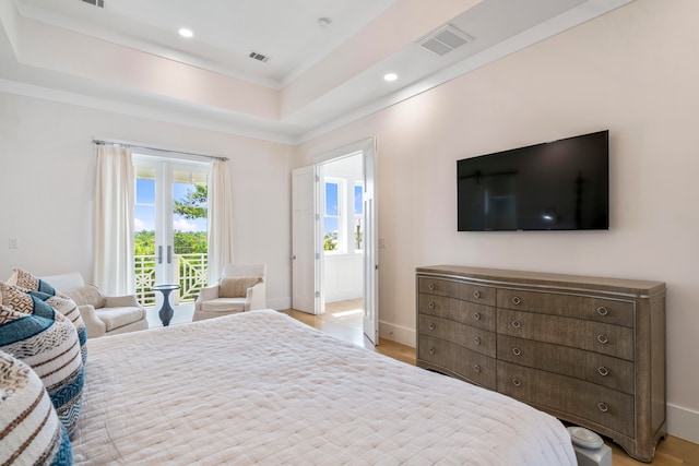 bedroom with a tray ceiling, light hardwood / wood-style flooring, and connected bathroom