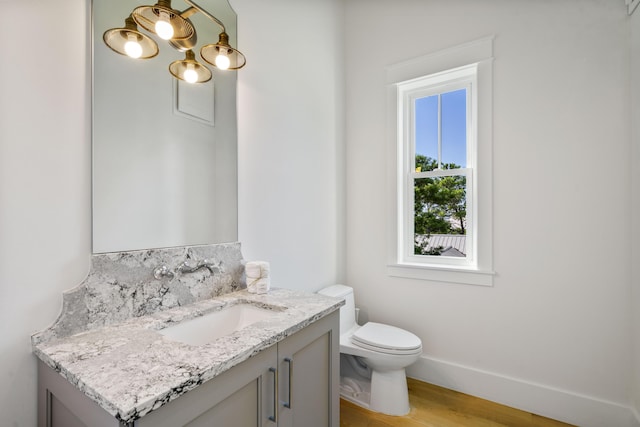 half bathroom featuring baseboards, toilet, vanity, and wood finished floors