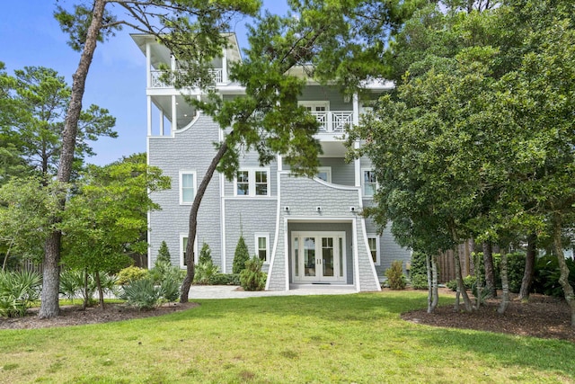 rear view of house with french doors, a balcony, and a yard