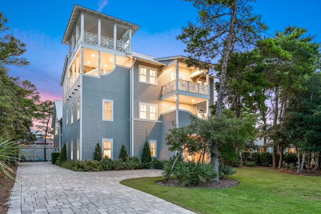 property exterior at dusk featuring a garage, a yard, and a balcony