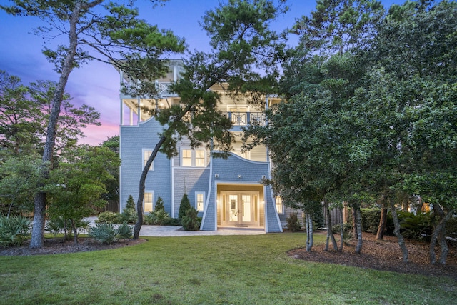 back of house at dusk featuring french doors, a yard, a balcony, and brick siding