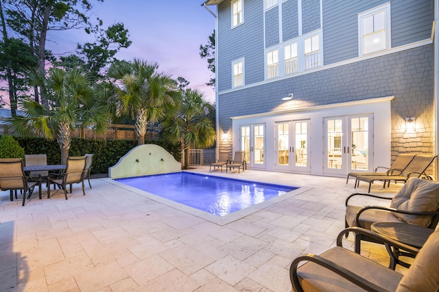 pool at dusk featuring a fenced in pool, fence, outdoor dining space, a patio area, and french doors