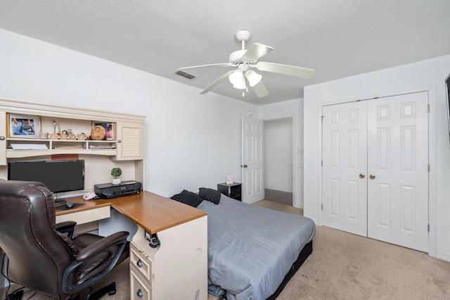 bedroom with ceiling fan, light colored carpet, a closet, and a textured ceiling