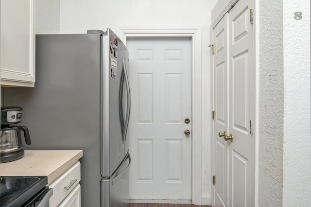 kitchen with white cabinets, range, and stainless steel refrigerator