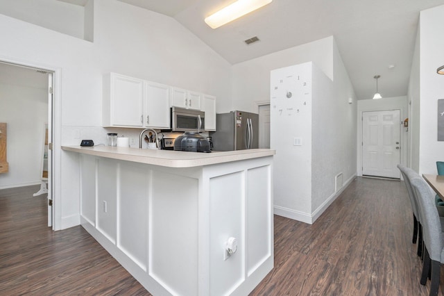 kitchen featuring appliances with stainless steel finishes, decorative light fixtures, lofted ceiling, white cabinets, and dark wood-type flooring