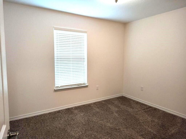 empty room featuring dark colored carpet and baseboards