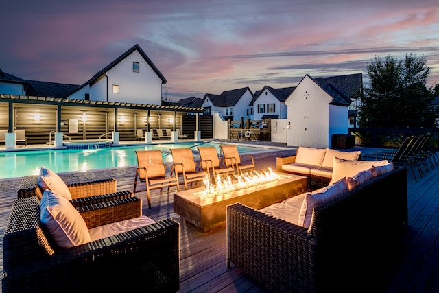 pool at dusk with a deck and an outdoor living space with a fire pit