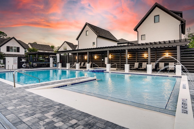 pool at dusk with pool water feature, a patio, and a hot tub