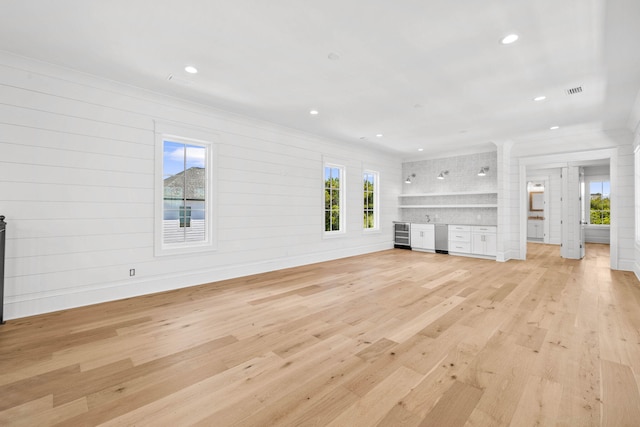 unfurnished living room with a healthy amount of sunlight, wooden walls, and light hardwood / wood-style floors