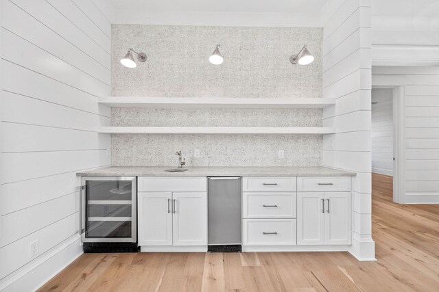 kitchen featuring wood walls, wine cooler, sink, white cabinets, and light hardwood / wood-style floors