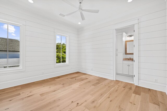 empty room with ceiling fan, wood walls, sink, and light hardwood / wood-style floors