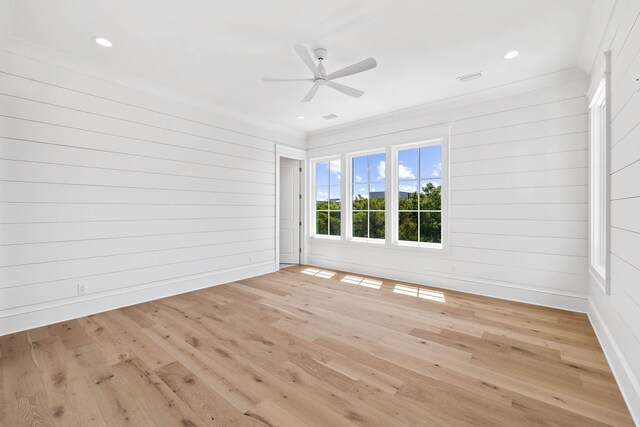 empty room featuring light wood-type flooring, crown molding, wood walls, and ceiling fan