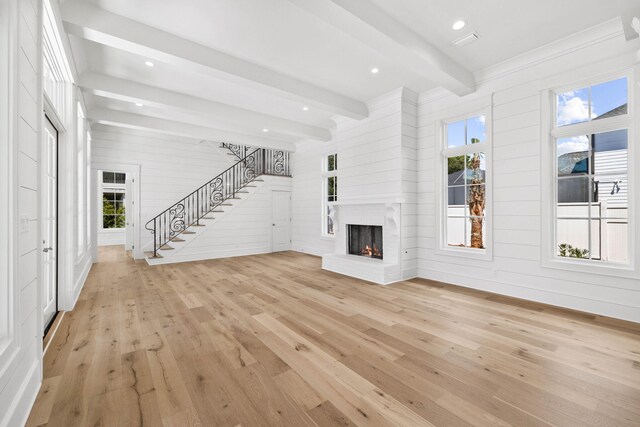 unfurnished living room with light wood-type flooring, wood walls, and beam ceiling