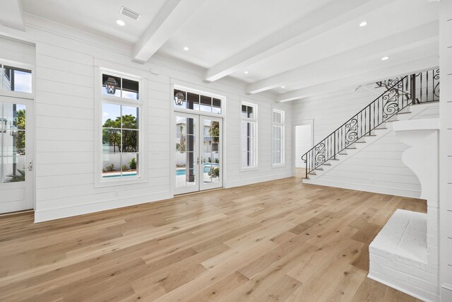 living room with light wood-type flooring, wood walls, a wealth of natural light, and beamed ceiling