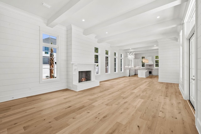 unfurnished living room with wooden walls, a chandelier, light hardwood / wood-style flooring, a brick fireplace, and beam ceiling