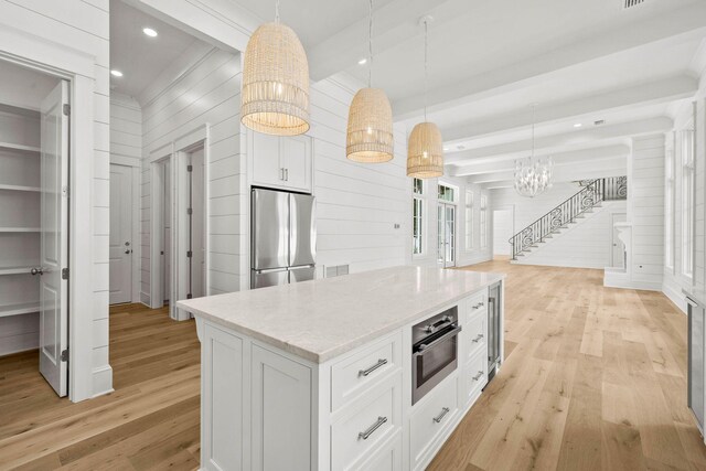 kitchen with decorative light fixtures, stainless steel appliances, wooden walls, and light hardwood / wood-style floors