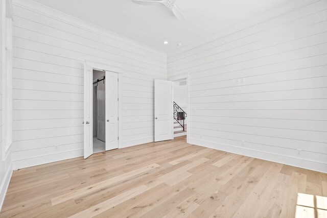 unfurnished bedroom featuring light wood-type flooring, ceiling fan, and wooden walls