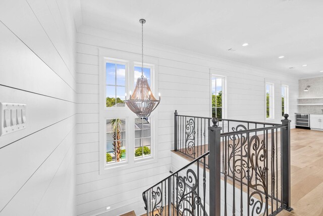 hallway featuring plenty of natural light, an inviting chandelier, wine cooler, and light wood-type flooring