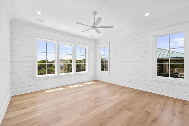 spare room with ceiling fan, wood walls, and light hardwood / wood-style floors