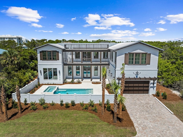 rear view of property featuring a lawn, decorative driveway, fence, an attached garage, and a balcony