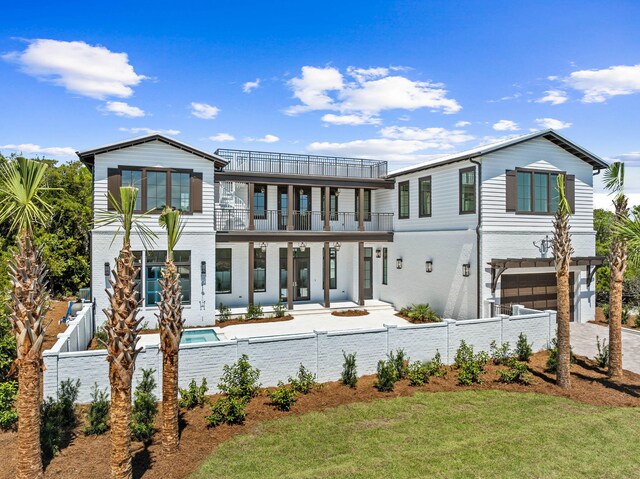 rear view of property featuring a balcony, driveway, a garage, a fenced front yard, and brick siding