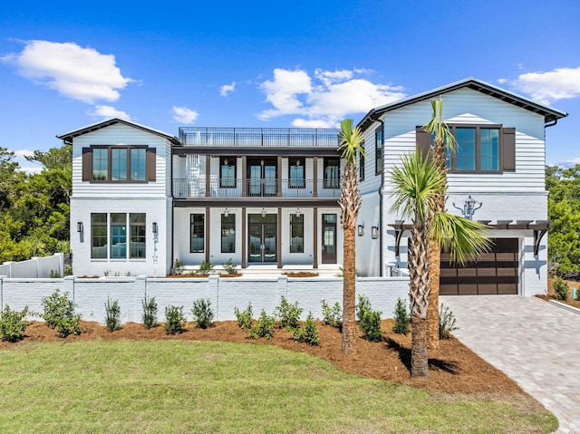 view of front of house featuring a front lawn, fence, decorative driveway, a balcony, and an attached garage