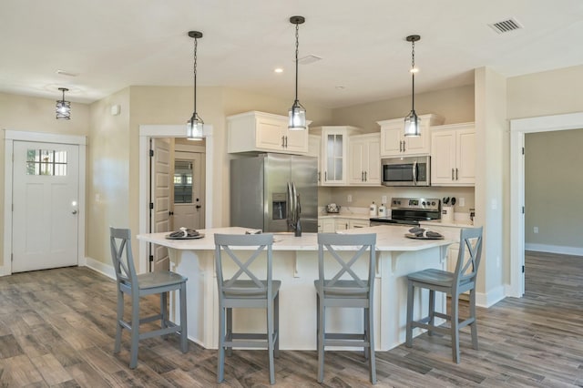 kitchen featuring a large island with sink, white cabinetry, hanging light fixtures, and stainless steel appliances