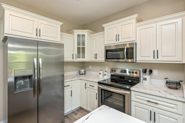 kitchen with white cabinets, light stone countertops, appliances with stainless steel finishes, and light hardwood / wood-style flooring