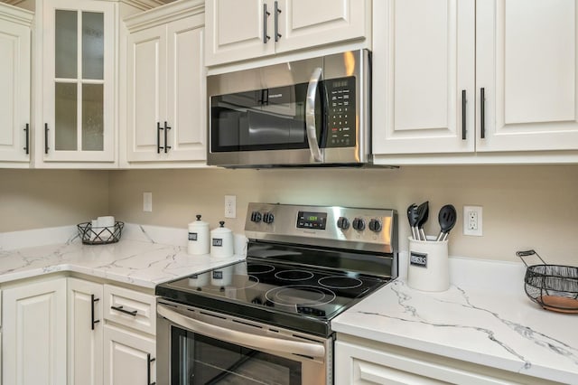 kitchen featuring stainless steel appliances, white cabinetry, and light stone counters