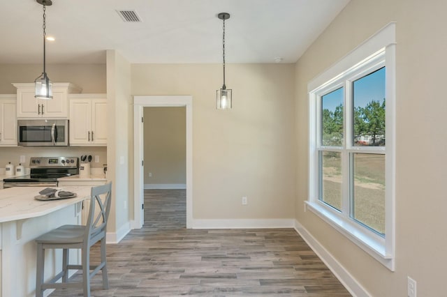 kitchen with white cabinetry, stainless steel appliances, light stone counters, pendant lighting, and light wood-type flooring